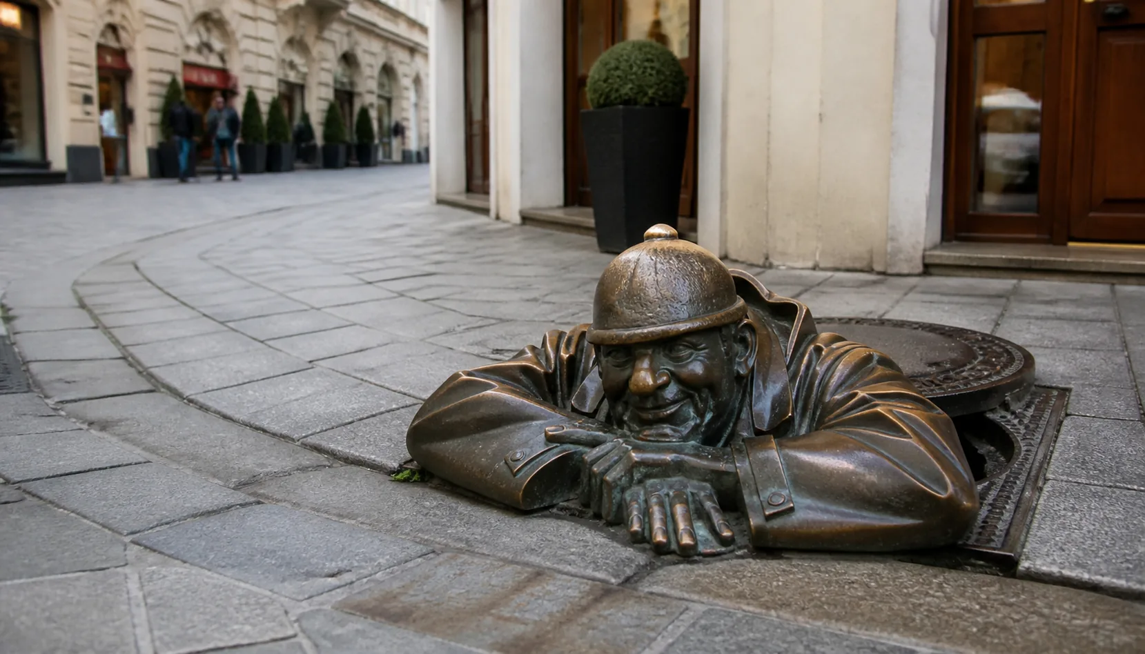 Čumil, the bronze "man at work", looking up from his manhole at passers-by on a cobbled Old Town street