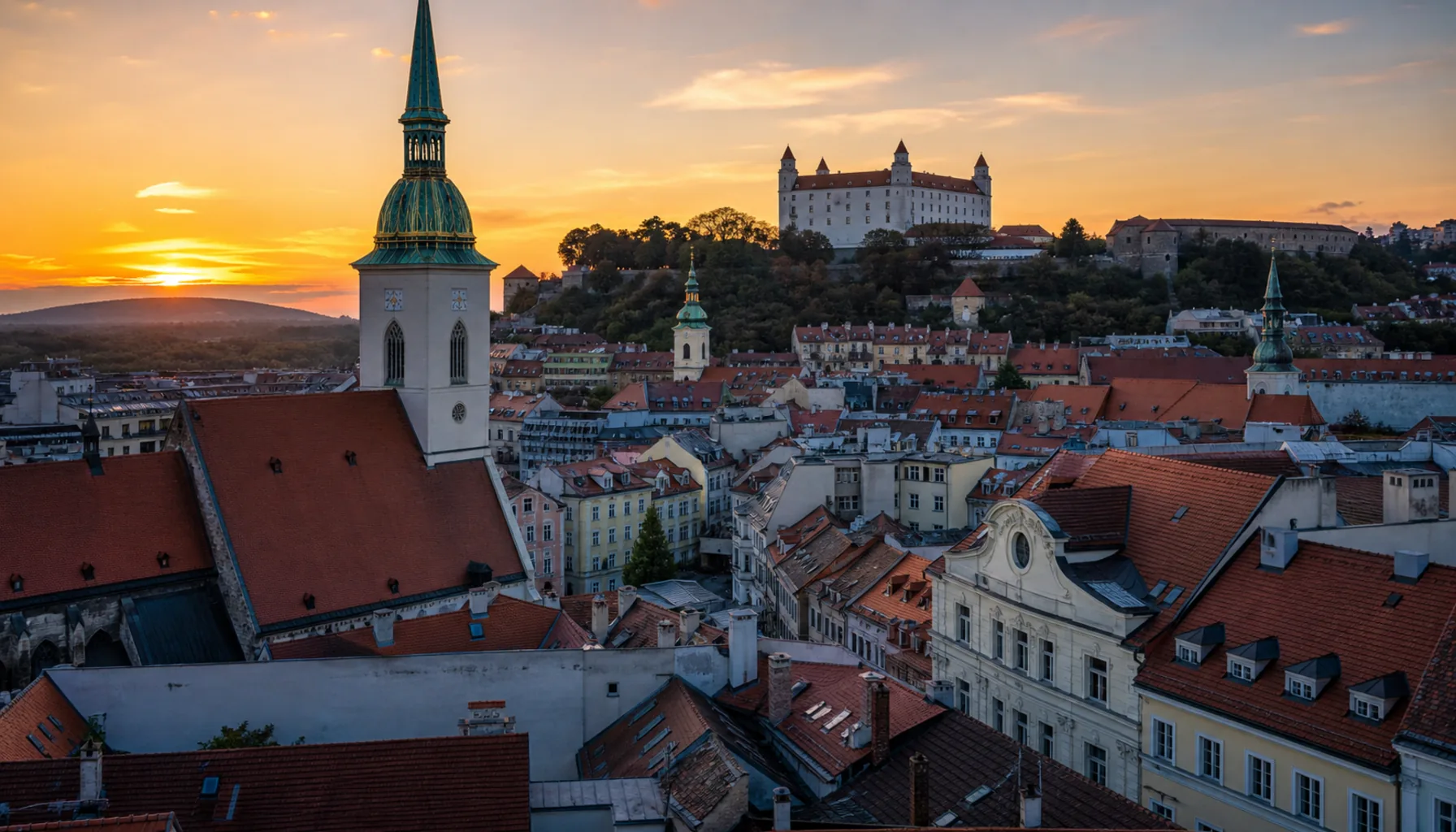 Old Town spires and rooftops with Bratislava Castle on its hill behind, evening light settling over the capital