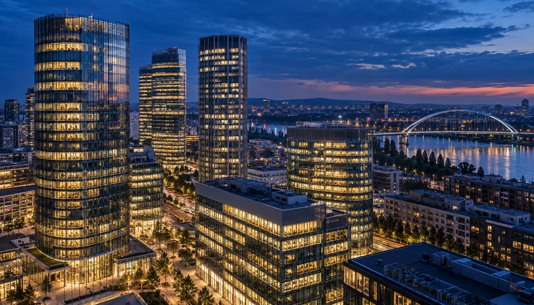 The bank towers of Mlynské nivy in Bratislava at dusk — glass façades lit floor by floor, the Danube behind.