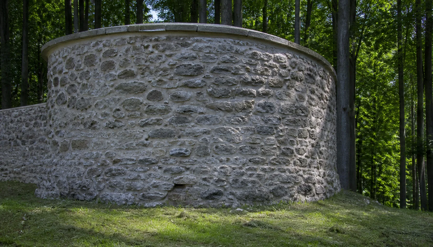 A consolidated bastion of the outer defences, stone and grass among the trees