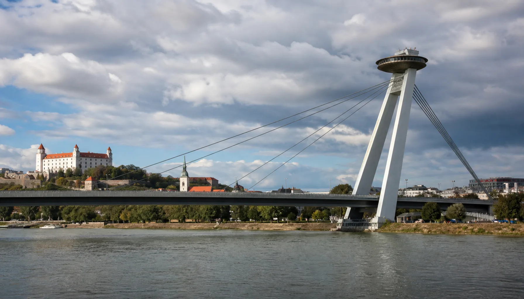 The cable-stayed bridge and its pylon seen from the Petržalka bank, with the castle and Old Town beyond the water