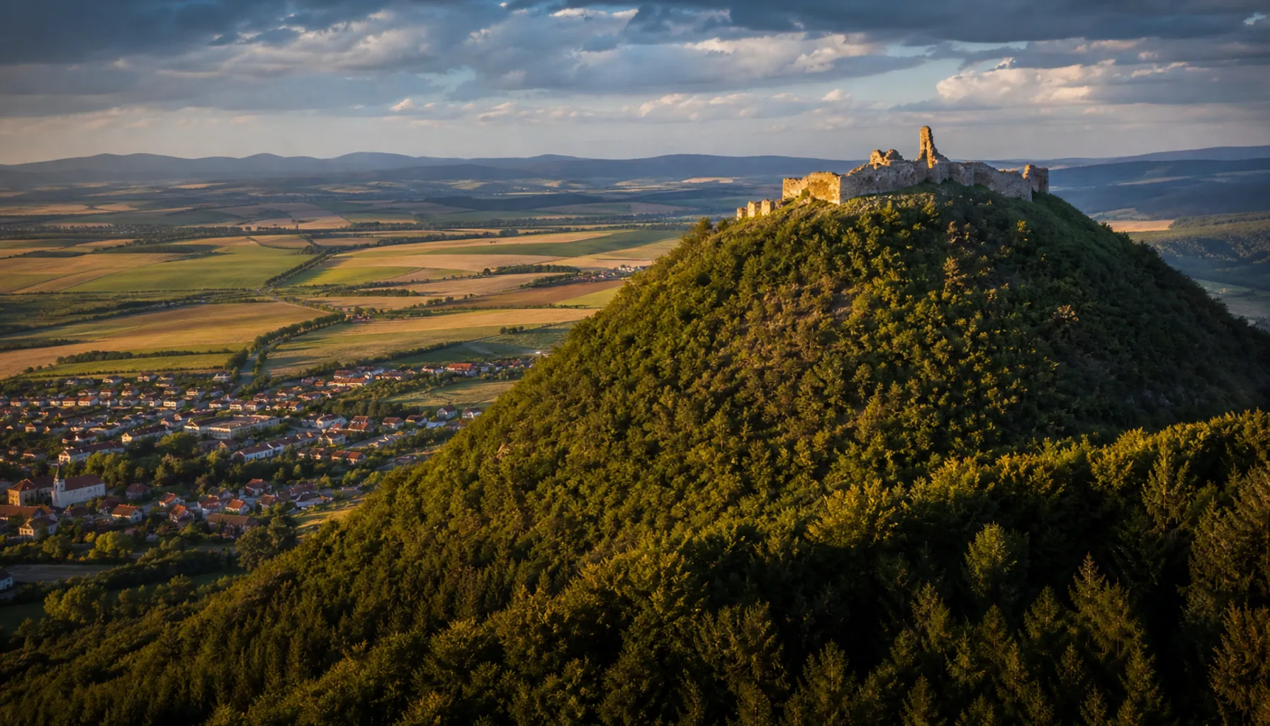Šariš Castle on its wooded cone above Veľký Šariš, seen from the Prešov basin in late afternoon light