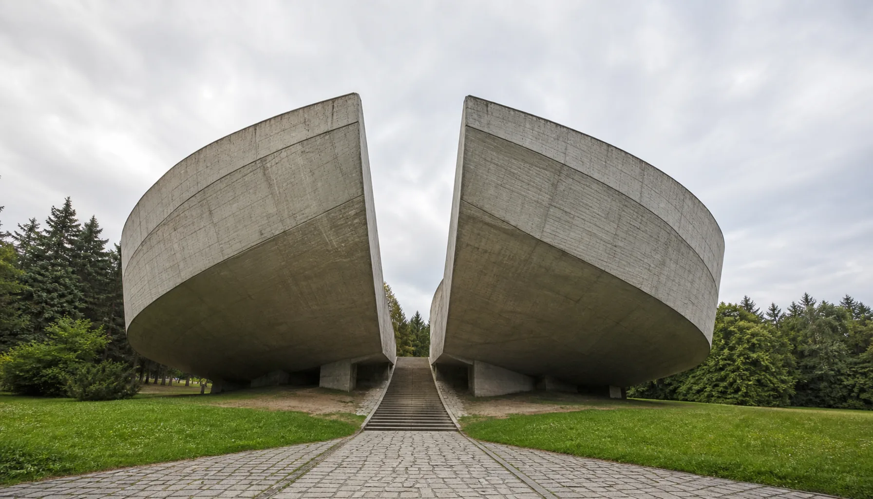 The Museum of the Slovak National Uprising — two curved concrete shells leaning apart, with the paved way running between them