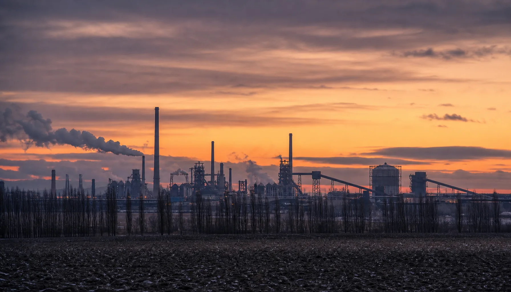 The ironworks horizon west of the city at dusk — stacks, gas holders and conveyor bridges on the plain toward Šaca