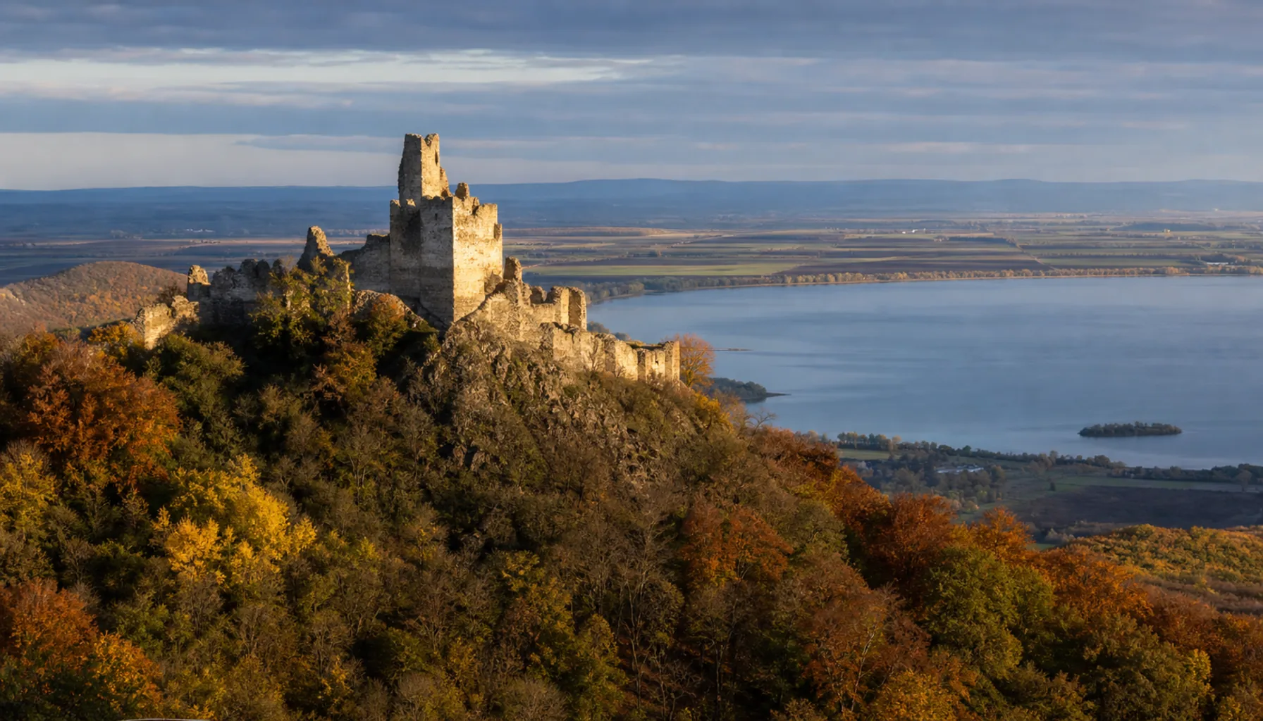 The broken walls of Vinné Castle on their wooded knoll, with the lake country of Zemplín opening out below