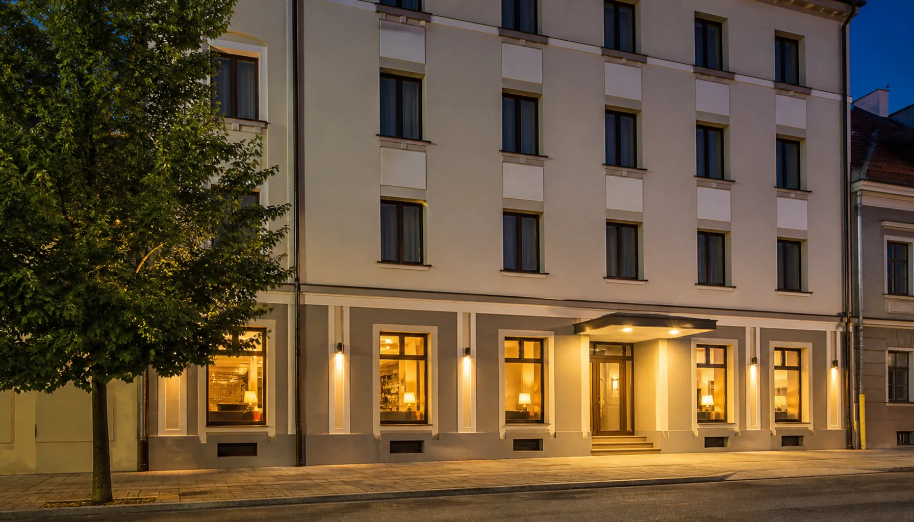 A hotel façade on a quiet street in central Nitra, warm light in the ground-floor windows