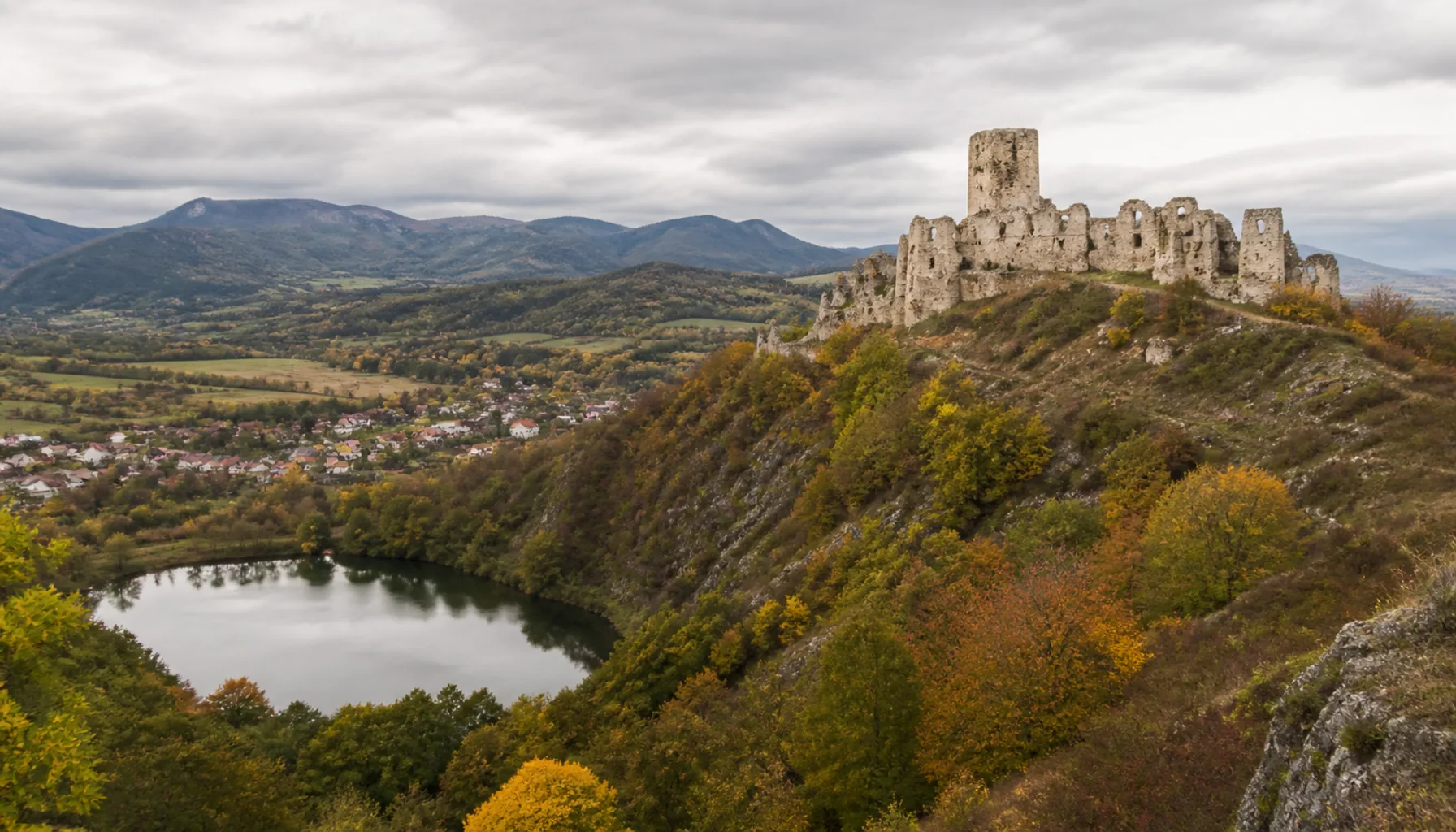 The ruins of Gýmeš Castle on the wooded ridge above Jelenec and its lake