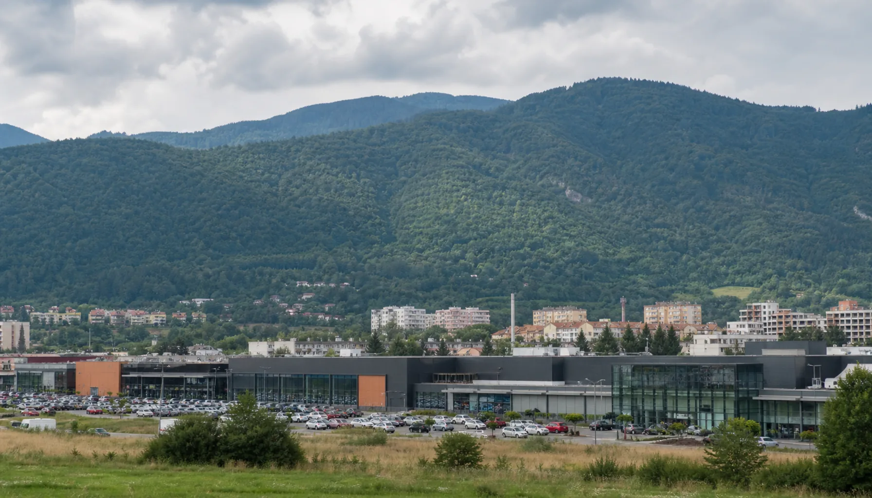 The modern retail edge of Banská Bystrica in the Hron valley, low glass-fronted centres below wooded ridges