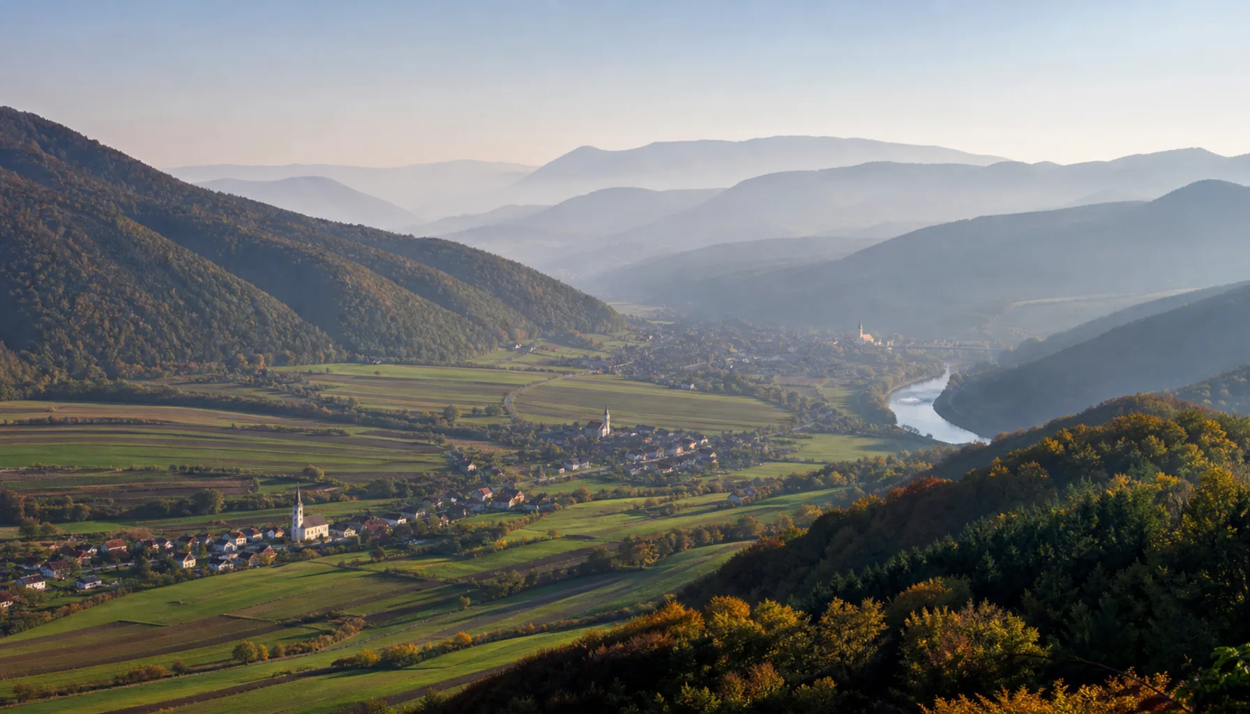 A wide view over the Váh valley, its villages and field strips backed by receding forested ridges